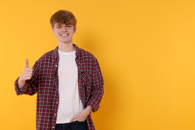 Teenage boy showing thumb up on orange background. Space for text