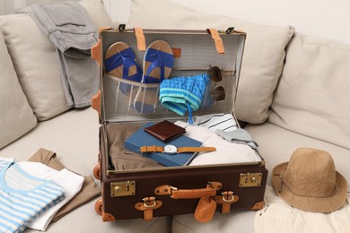 Photo of Open suitcase with different men clothes and accessories on sofa