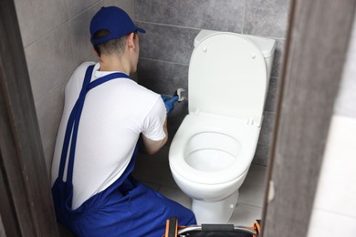 Plumber with spanner repairing toilet bowl in water closet