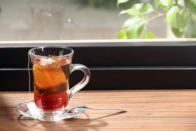 Photo of Glass cup of hot tea on wooden window sill. Space for text