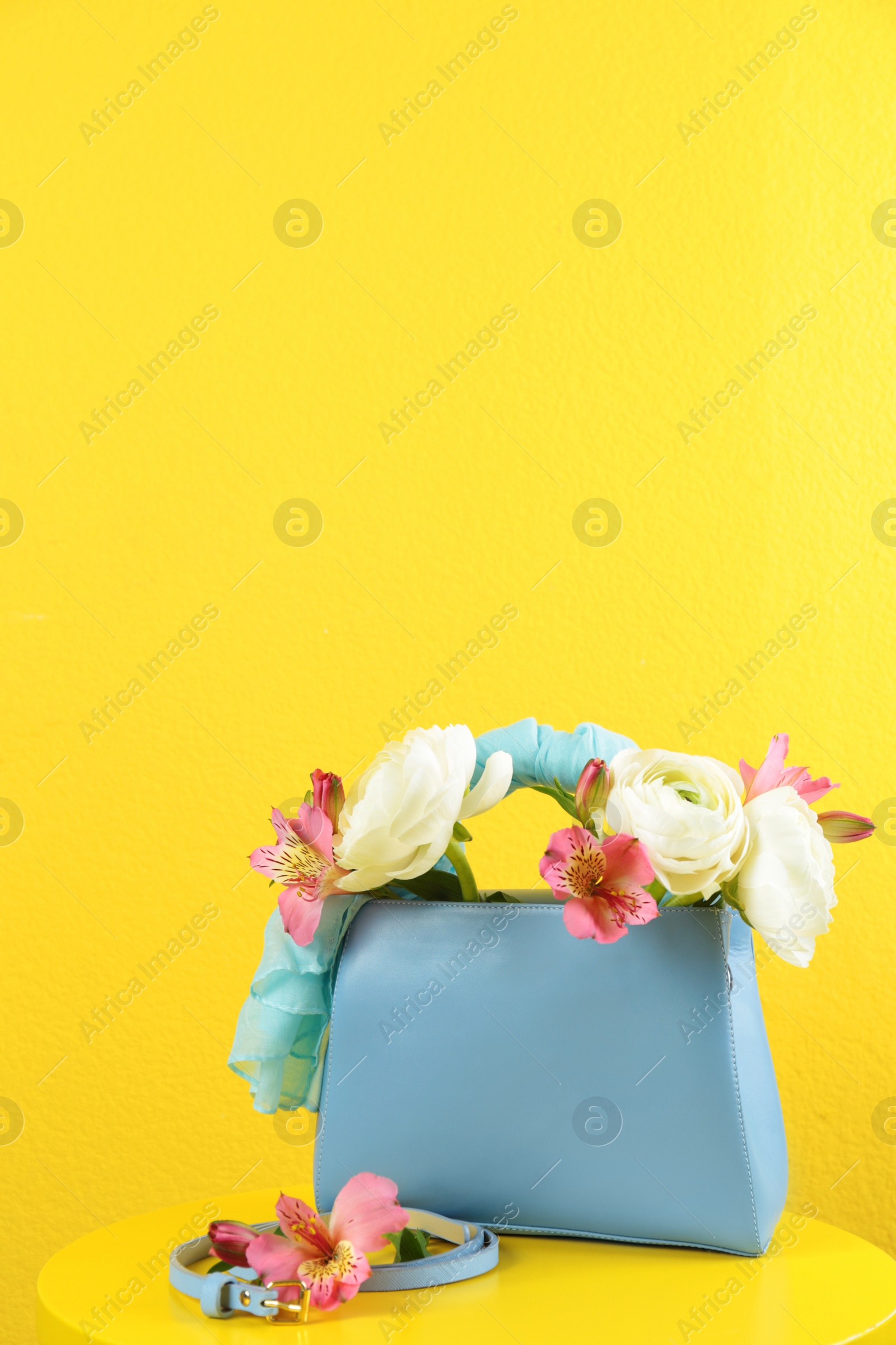 Photo of Elegant handbag with flowers and belt on table against yellow background, space for text