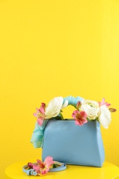 Photo of Elegant handbag with flowers and belt on table against yellow background, space for text