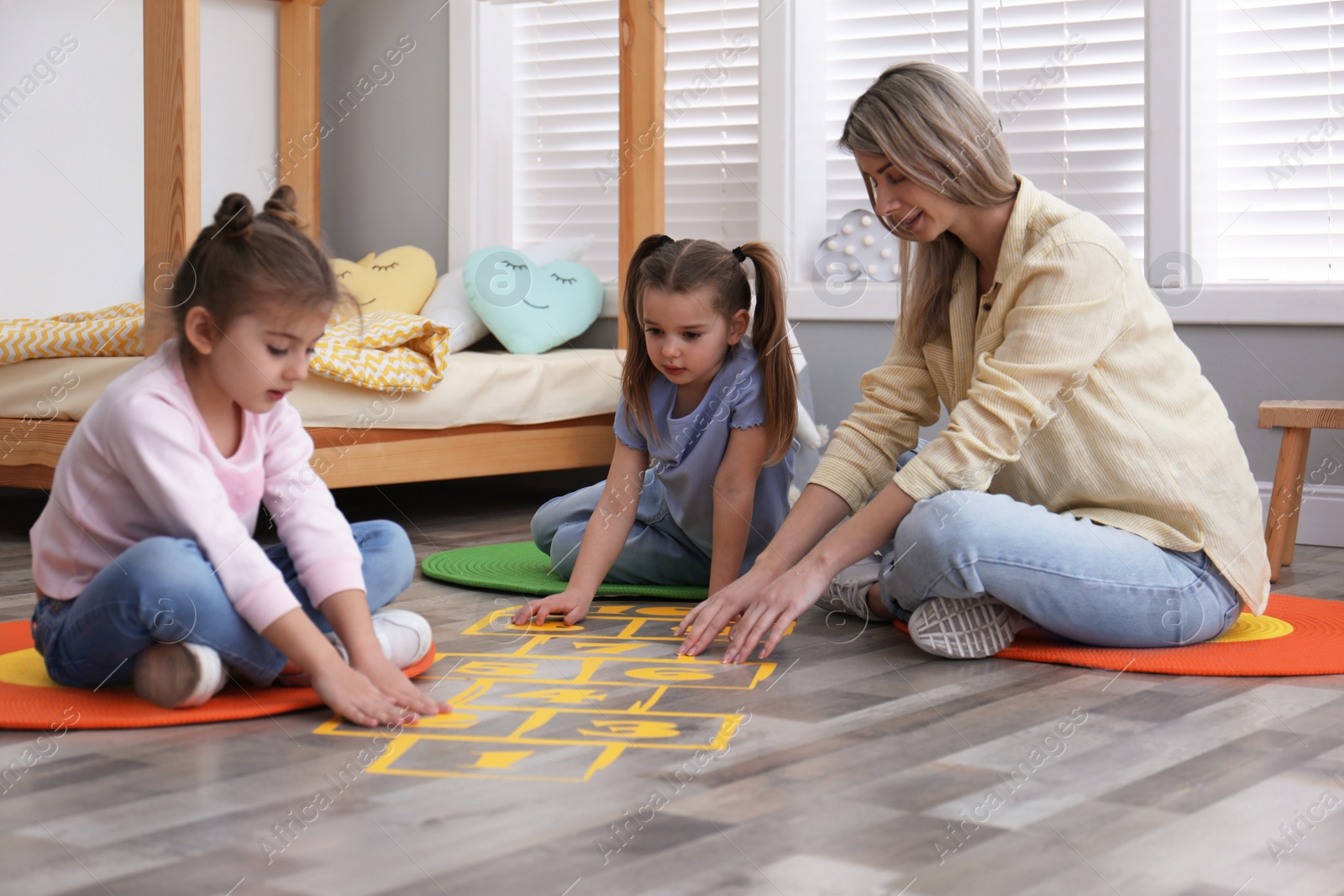 Photo of Mother and little girls taping sticker hopscotch on floor at home