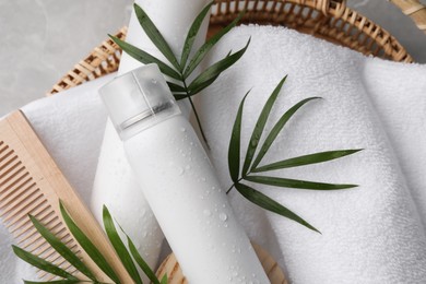 Dry shampoo sprays, towel and wooden comb with green leaves in wicker basket on table, top view