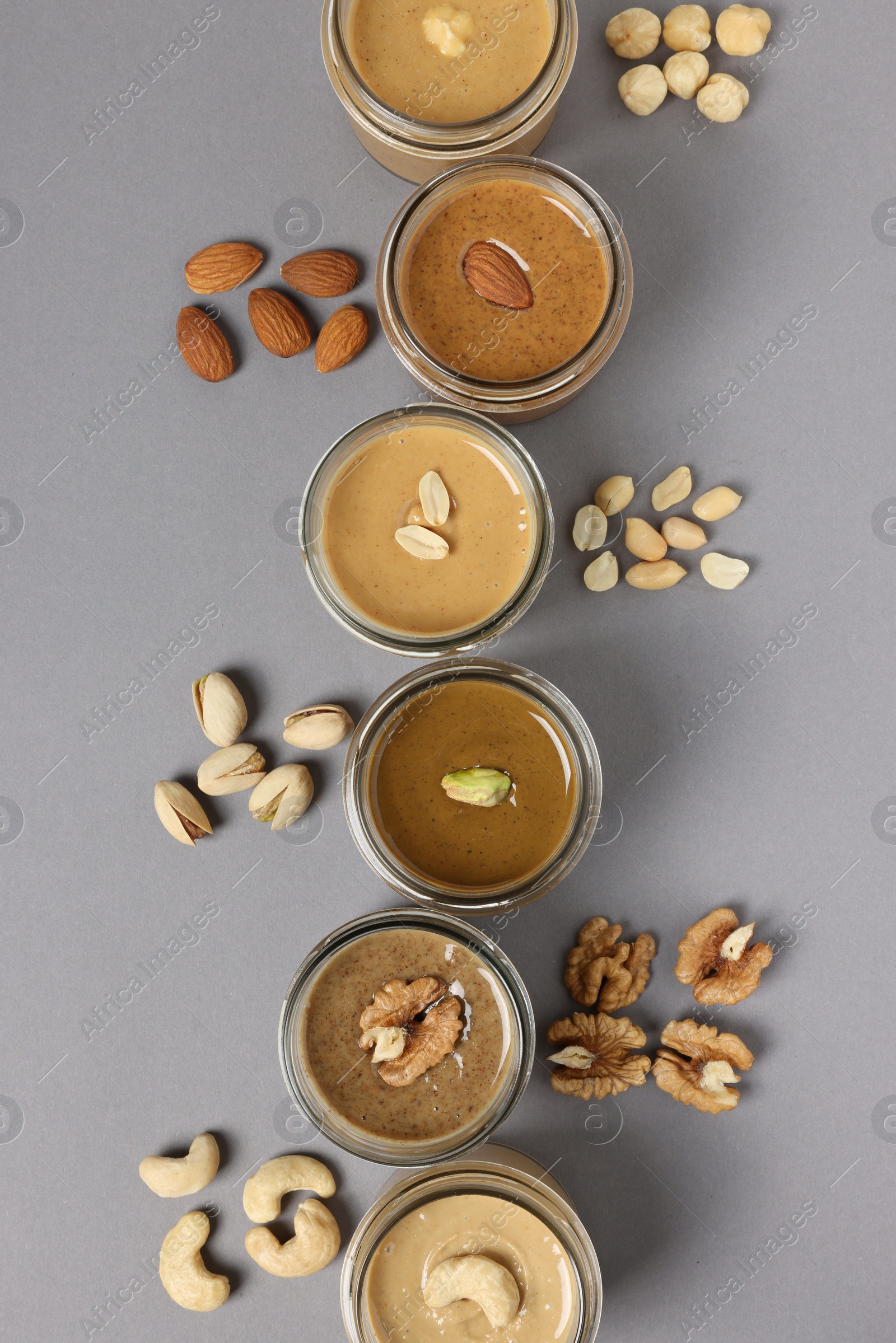 Photo of Tasty nut butters in jars and raw nuts on gray table, flat lay