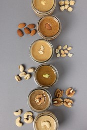 Photo of Tasty nut butters in jars and raw nuts on gray table, flat lay