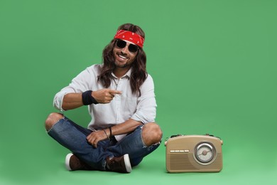 Photo of Stylish hippie man in sunglasses pointing at something on green background