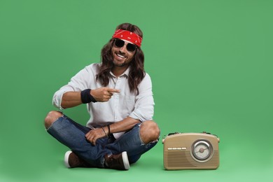 Stylish hippie man in sunglasses pointing at something on green background