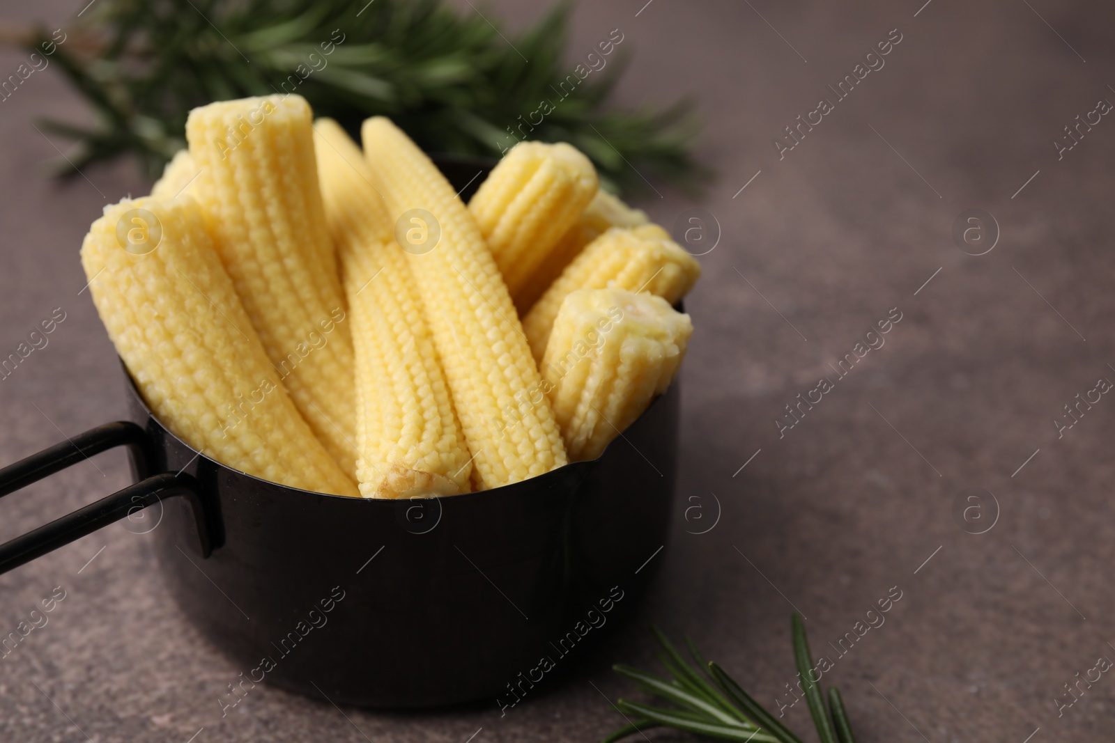 Photo of Tasty fresh yellow baby corns in dish on brown table, closeup. Space for text