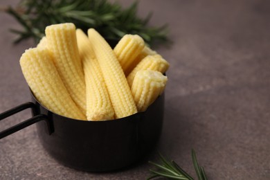 Photo of Tasty fresh yellow baby corns in dish on brown table, closeup. Space for text