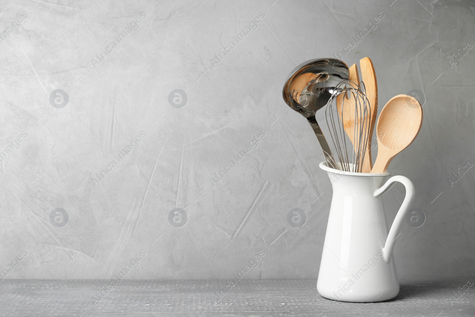 Photo of Jug with kitchen utensils on wooden table against light grey background. Space for text