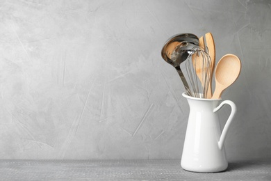 Photo of Jug with kitchen utensils on wooden table against light grey background. Space for text