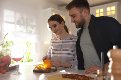 Photo of Lovely young couple cooking pizza together in kitchen