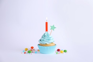 Photo of Delicious birthday cupcake with burning candle and candies on light grey background