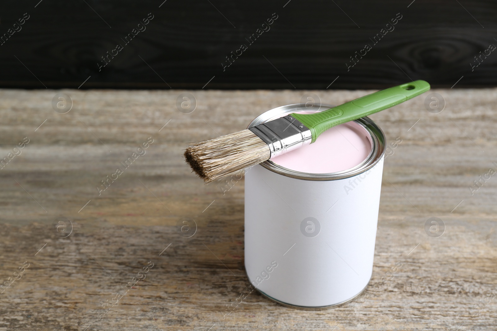 Photo of Can of pale pink paint with brush on wooden table