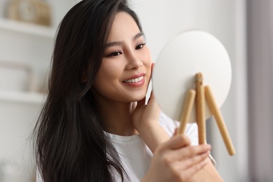 Woman with perfect skin looking at mirror indoors