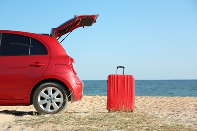 Modern car and bright suitcase on sand near sea. Beach accessories