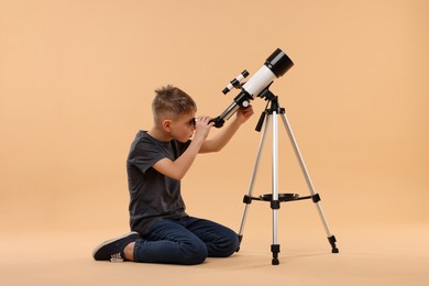 Photo of Little boy looking at stars through telescope on beige background