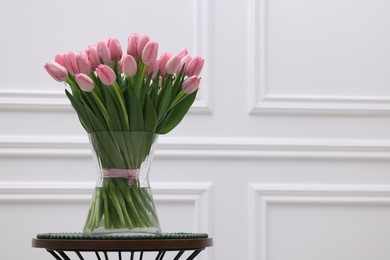 Bouquet of beautiful pink tulips in vase on table near white wall, space for text