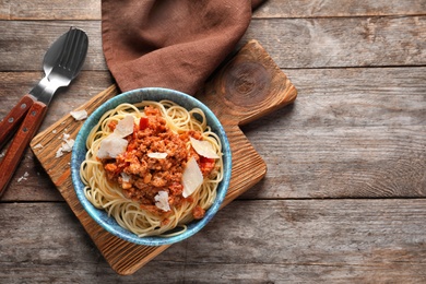 Bowl with delicious pasta bolognese on wooden table, top view