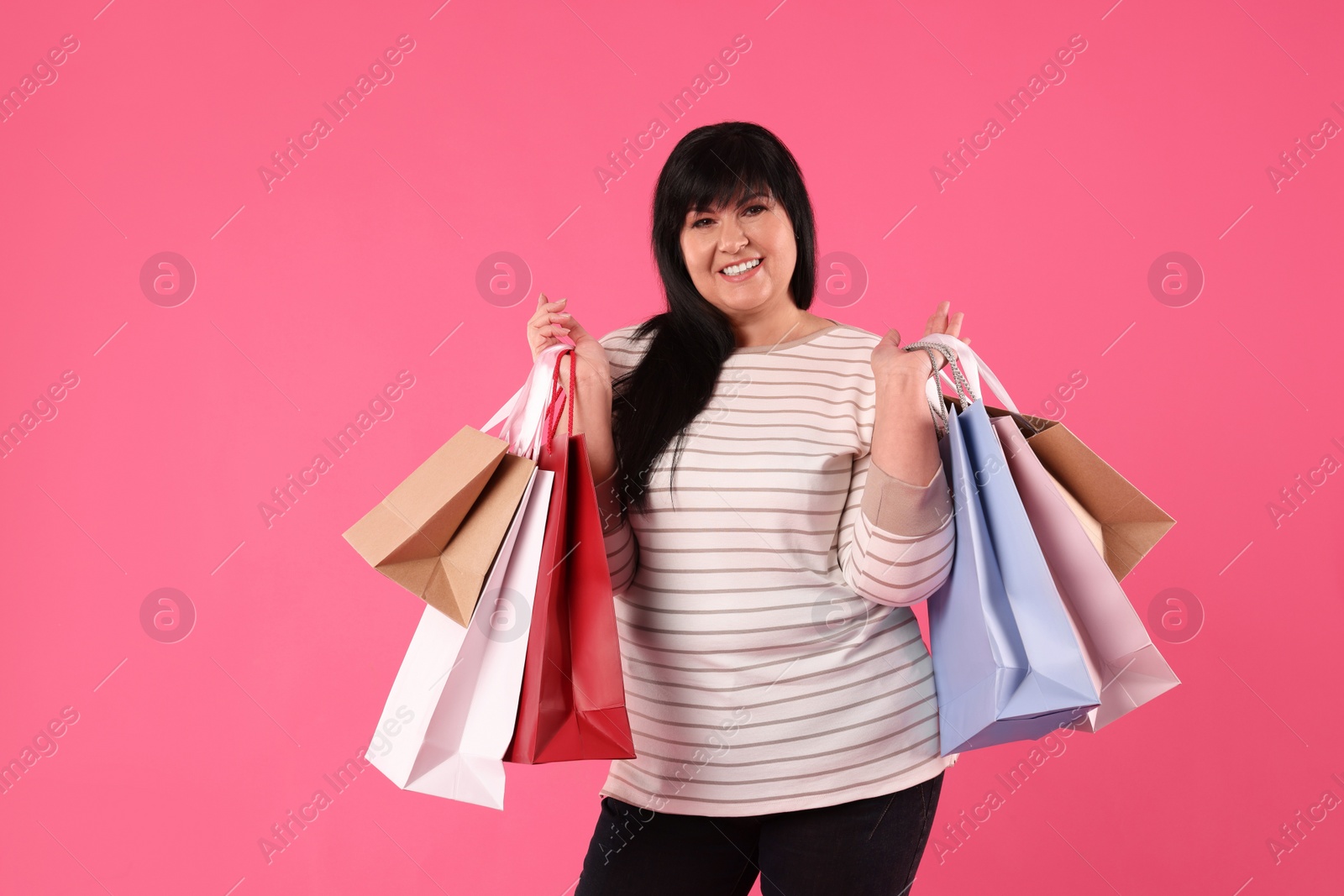 Photo of Beautiful overweight mature woman with shopping bags on pink background