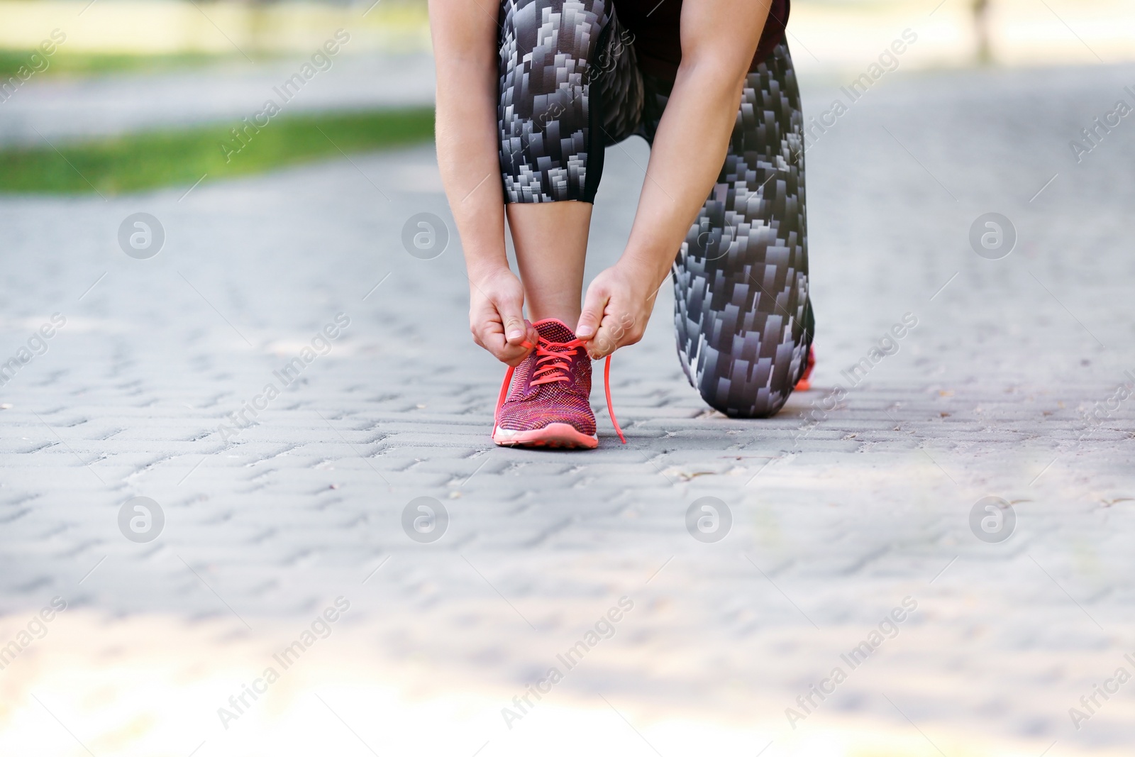 Photo of Young woman tying shoelaces before running outdoors, focus on legs