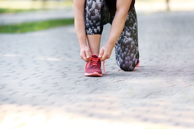 Photo of Young woman tying shoelaces before running outdoors, focus on legs