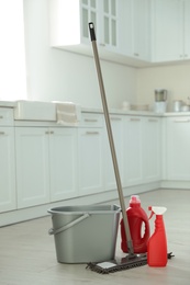 Photo of Mop, detergents and plastic bucket in kitchen. Cleaning supplies