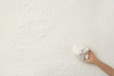 Wooden spoon on wheat flour, top view. Space for text