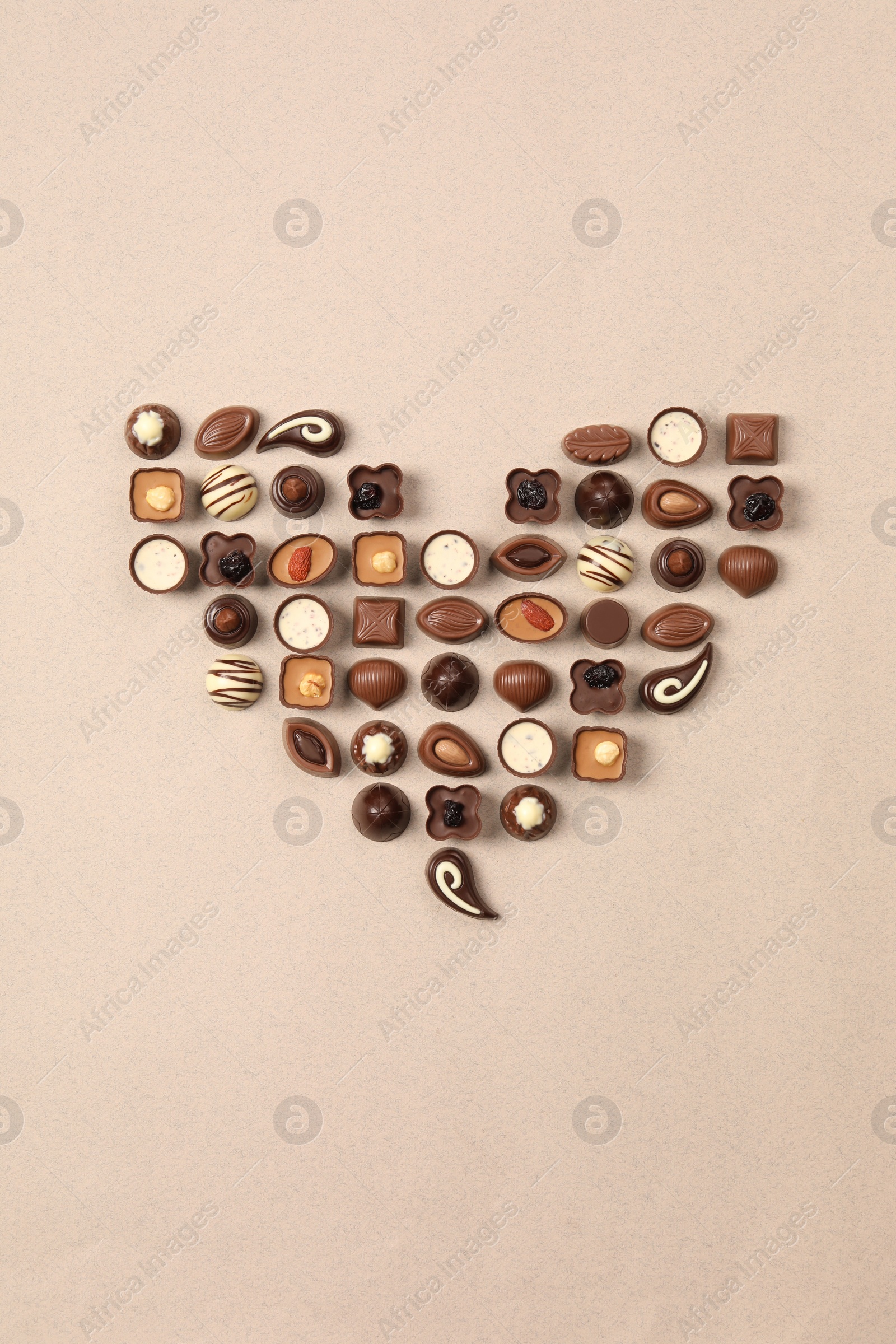 Photo of Heart made with delicious chocolate candies on beige background, top view