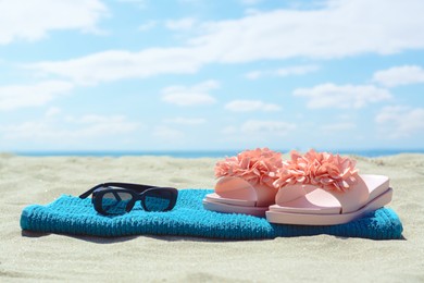 Towel, slippers and sunglasses on sand near sea. Beach accessories