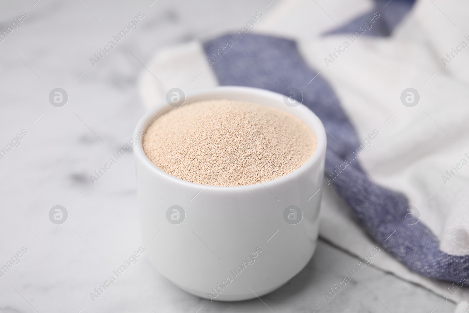 Photo of Granulated yeast in bowl on white marble table, closeup