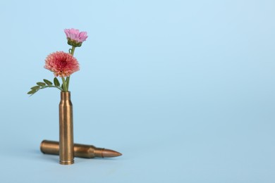 Photo of Bullets and beautiful chrysanthemum flowers on light blue background, space for text