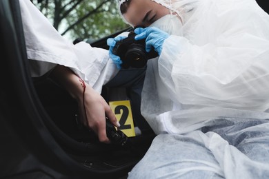 Photo of Criminologist taking photo of evidence at crime scene with dead body in car, closeup