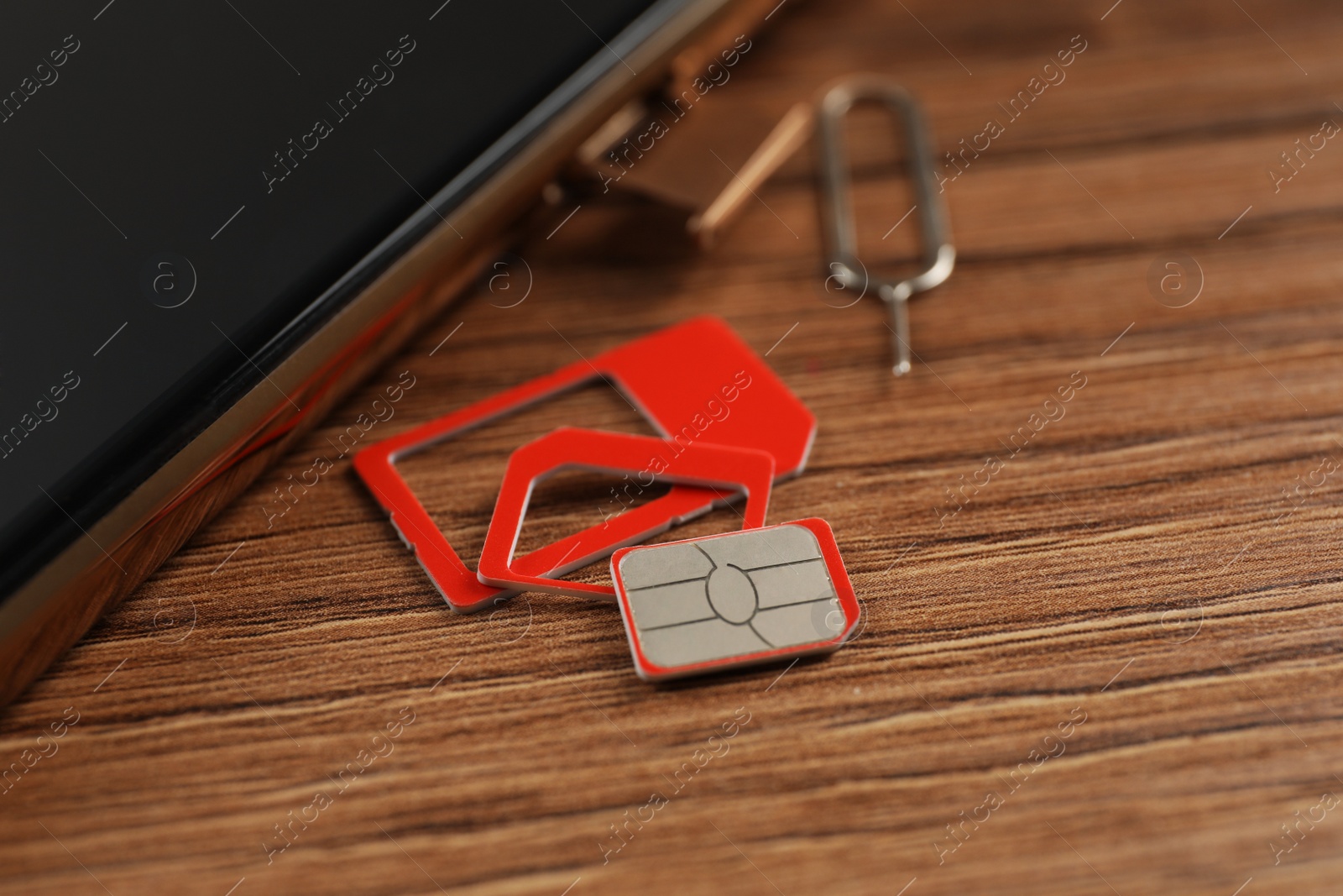 Photo of SIM card, mobile phone and ejector tool on wooden table, closeup