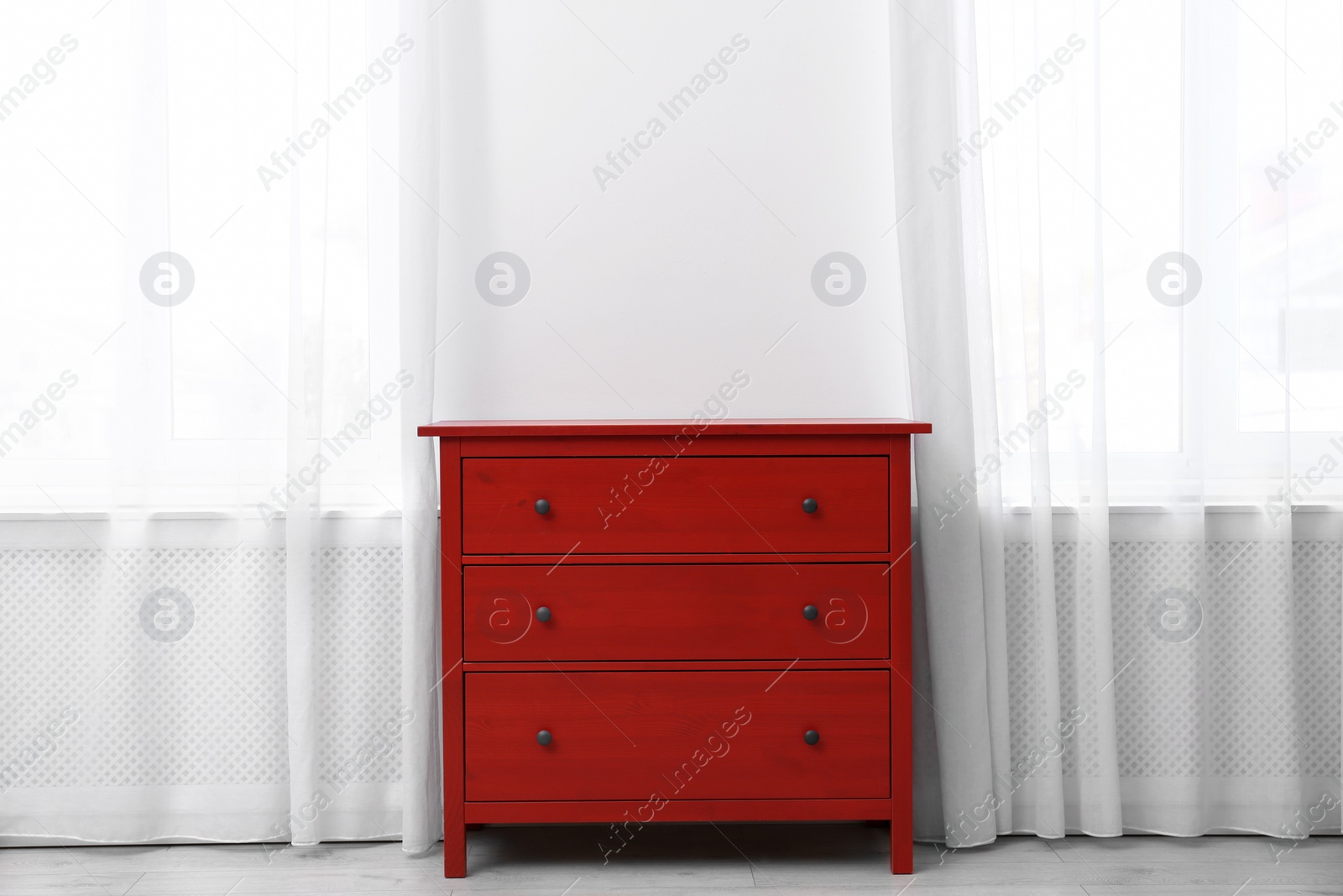 Photo of Red wooden chest of drawers near white wall indoors