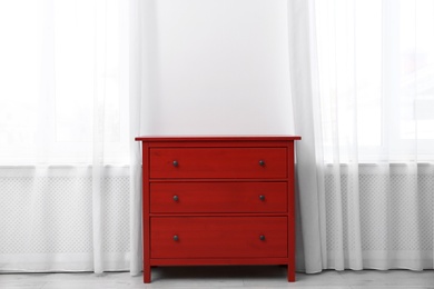 Red wooden chest of drawers near white wall indoors