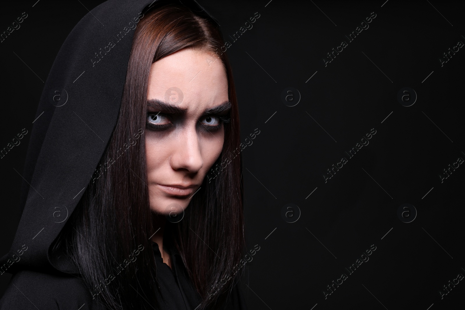 Photo of Mysterious witch with spooky eyes on black background, space for text