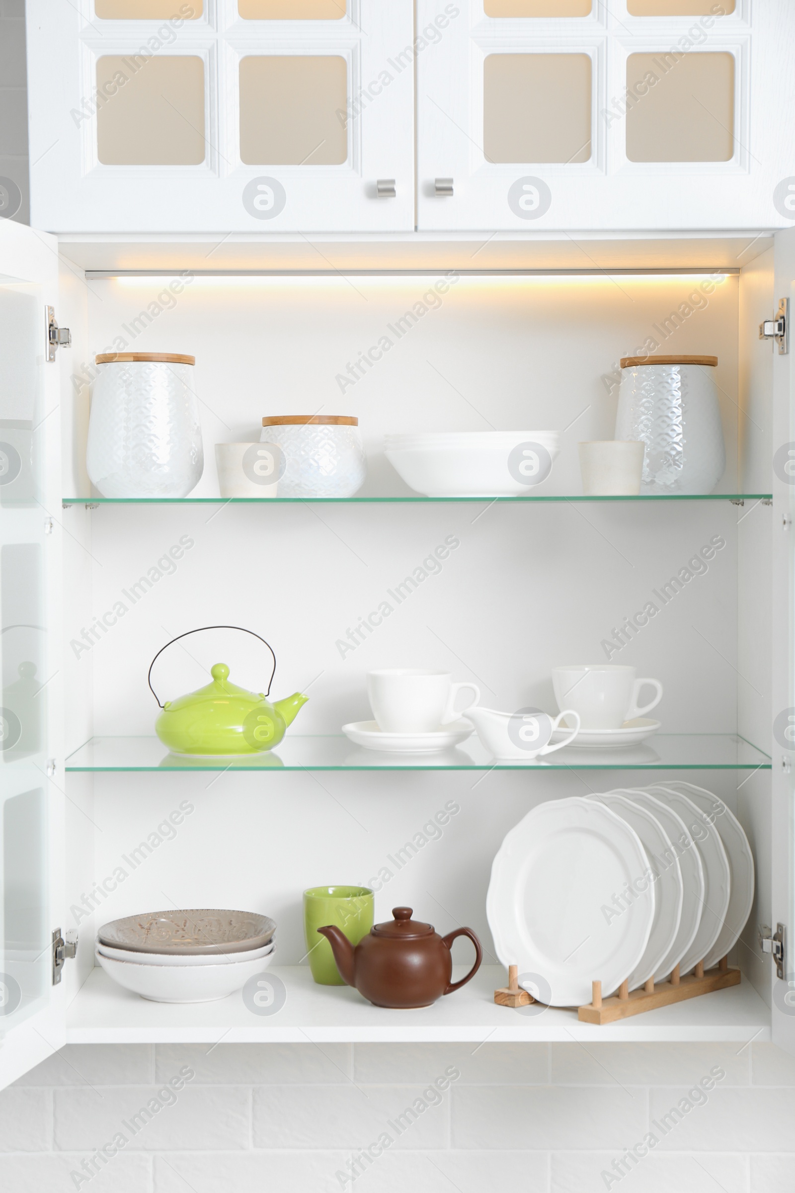 Photo of Open cabinet with different clean dishware in kitchen