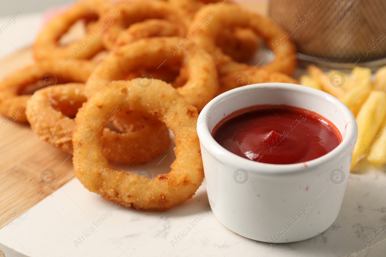 Photo of Tasty ketchup, fries and onion rings on board, closeup