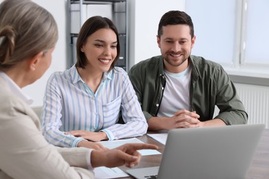 Young couple consulting insurance agent about pension plan at wooden table indoors