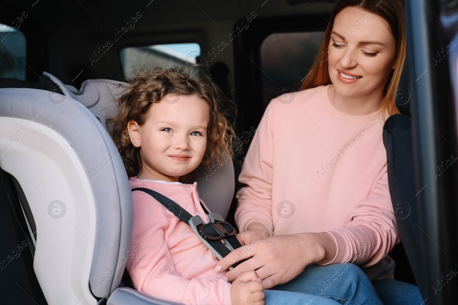 Photo of Mother fastening her daughter in child safety seat inside car