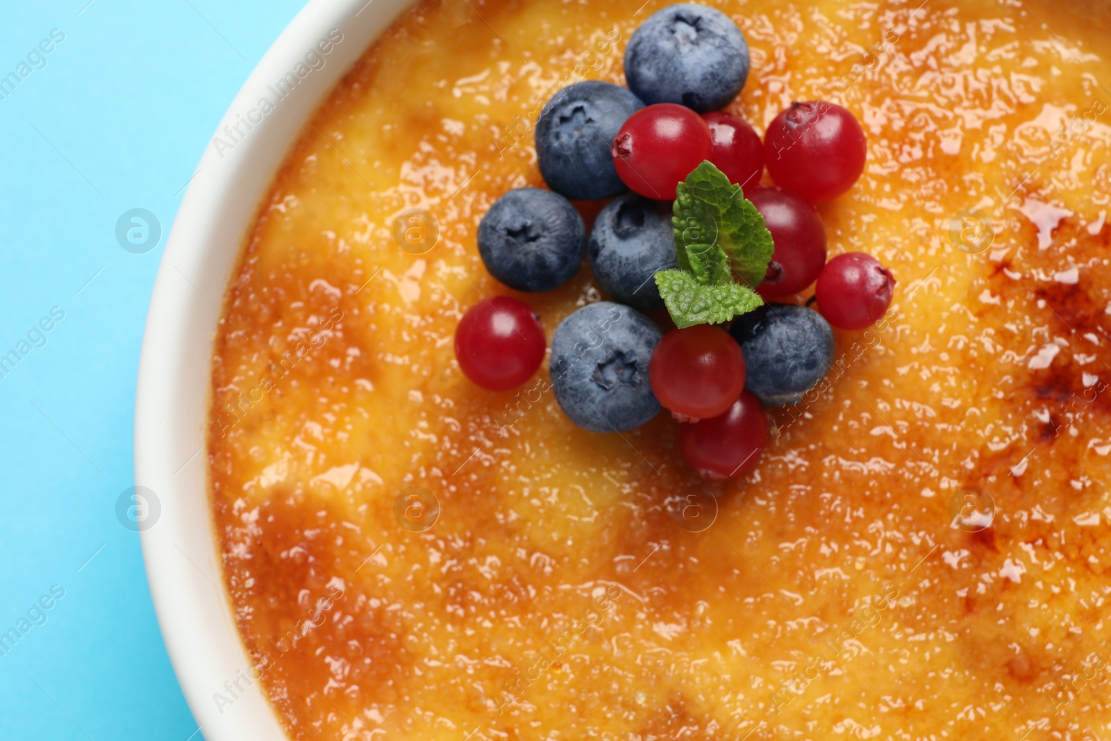 Photo of Delicious creme brulee with fresh berries and mint on light blue background, top view