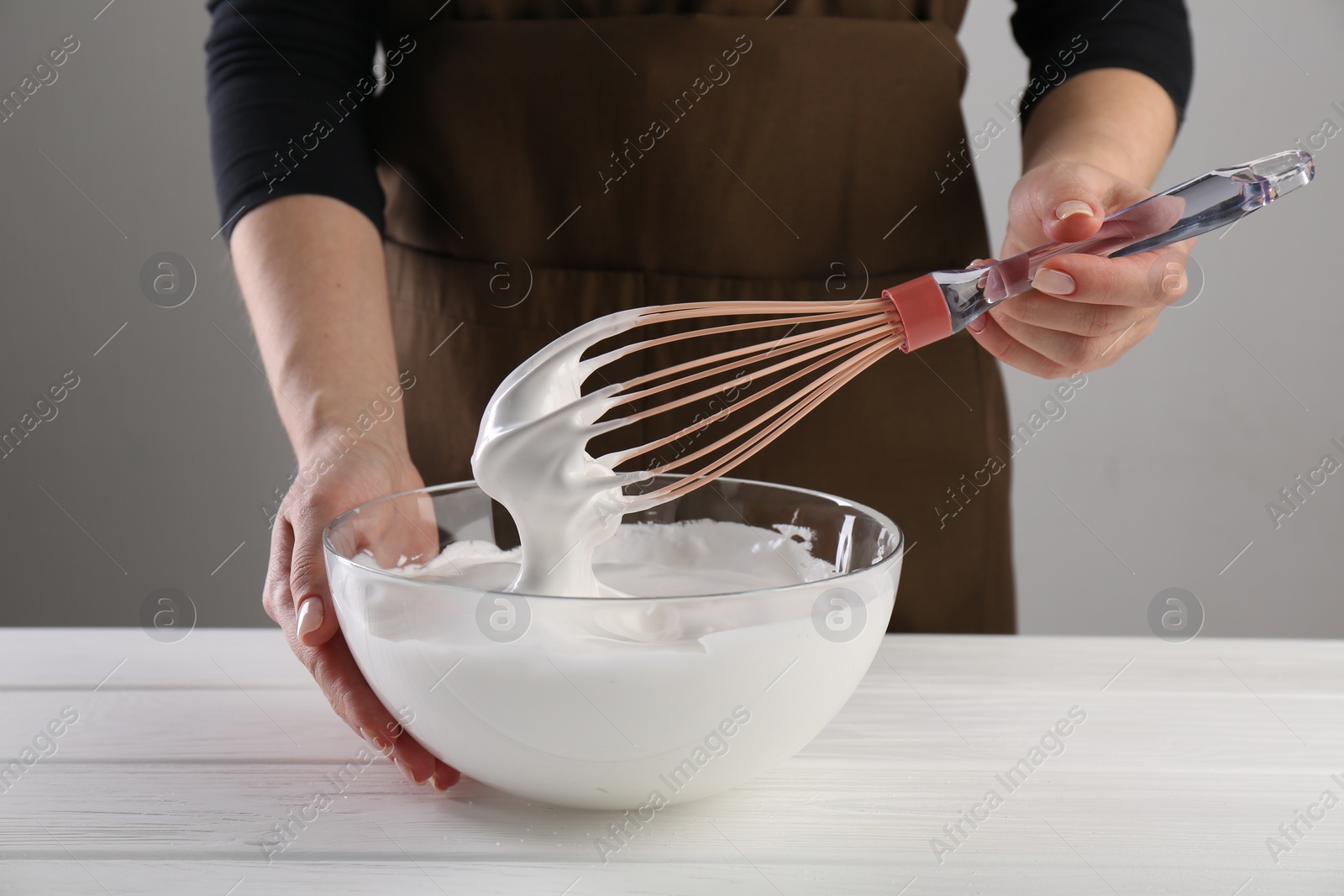 Photo of Woman making whipped cream with whisk at white wooden table, closeup