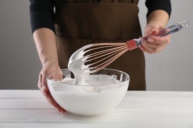 Woman making whipped cream with whisk at white wooden table, closeup