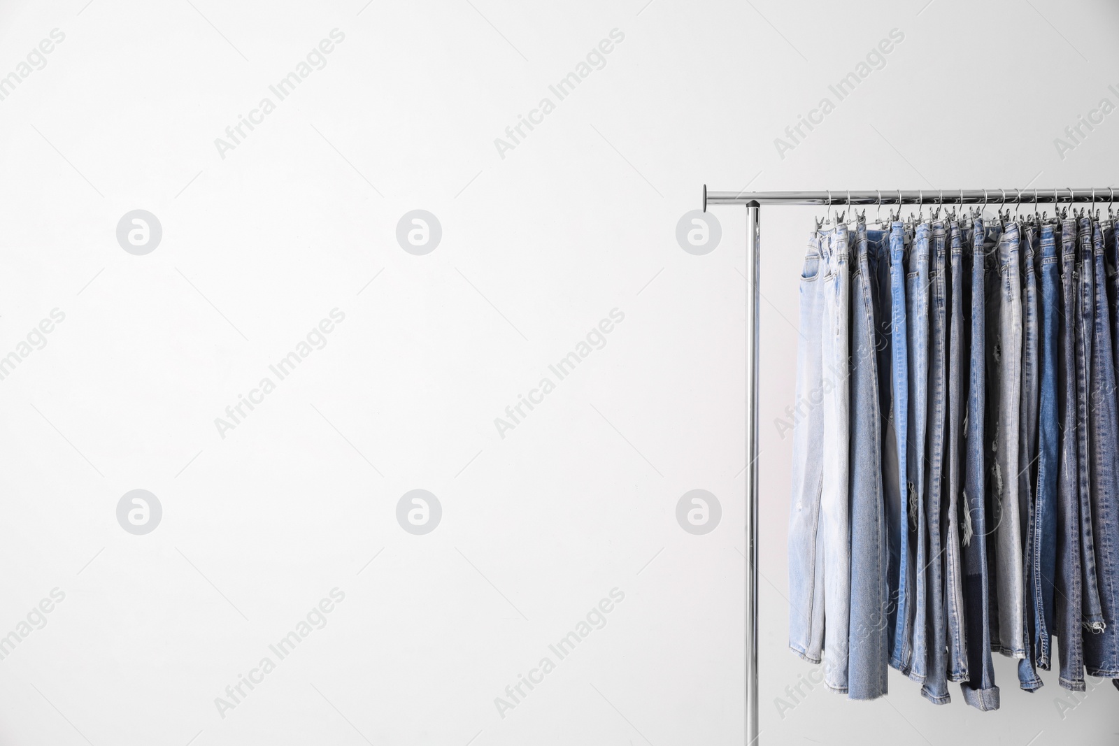 Photo of Rack with different jeans on light background. Space for text