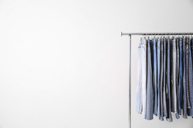 Rack with different jeans on light background. Space for text