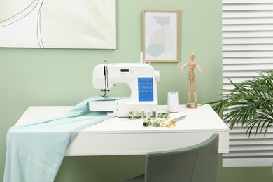 Photo of Modern sewing machine with cloth and craft accessories on white table near window in room