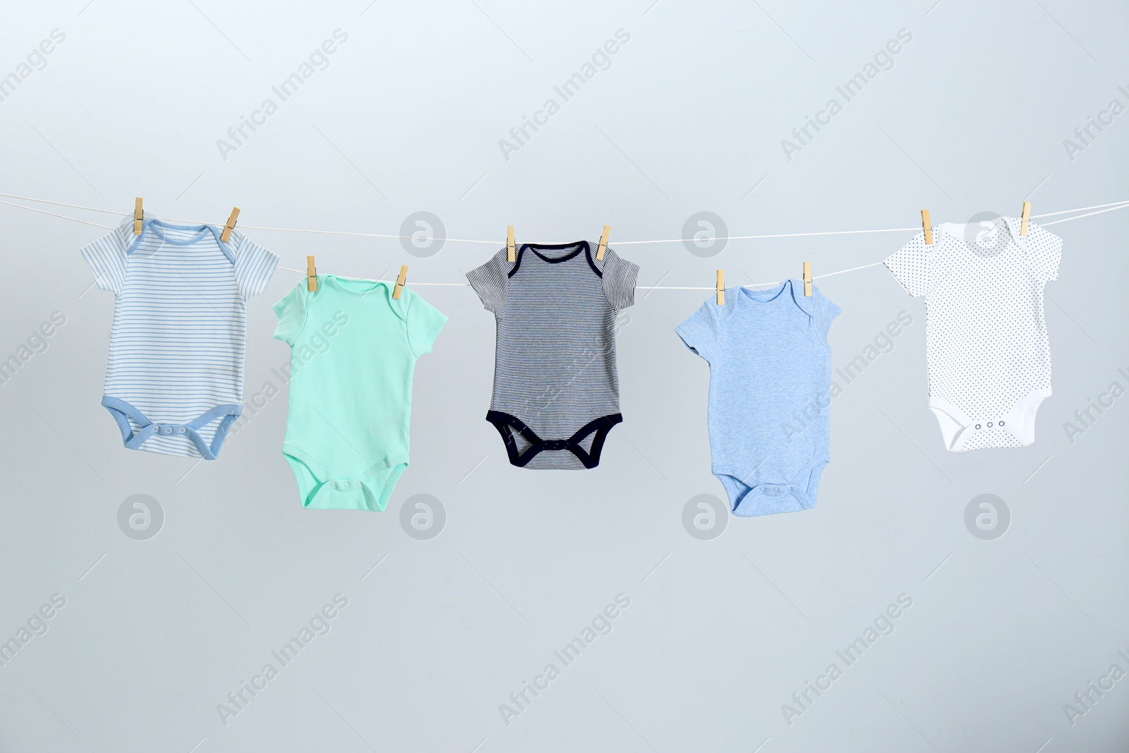 Photo of Different baby onesies hanging on clothes line against light grey background. Laundry day