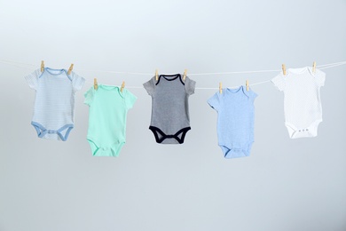Photo of Different baby onesies hanging on clothes line against light grey background. Laundry day